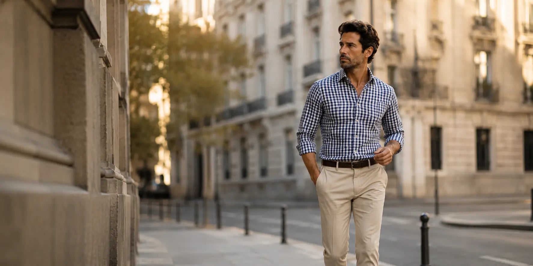 Hombre caminando por una calle europea con camisa de cuadros Vichy azul marino y pantalón beige en un entorno urbano elegante