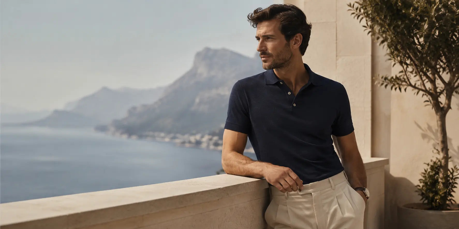 Hombre con polo azul marino y pantalón beige en una terraza mediterránea, mostrando cómo combinar un polo de hombre con estilo elegante y relajado.
