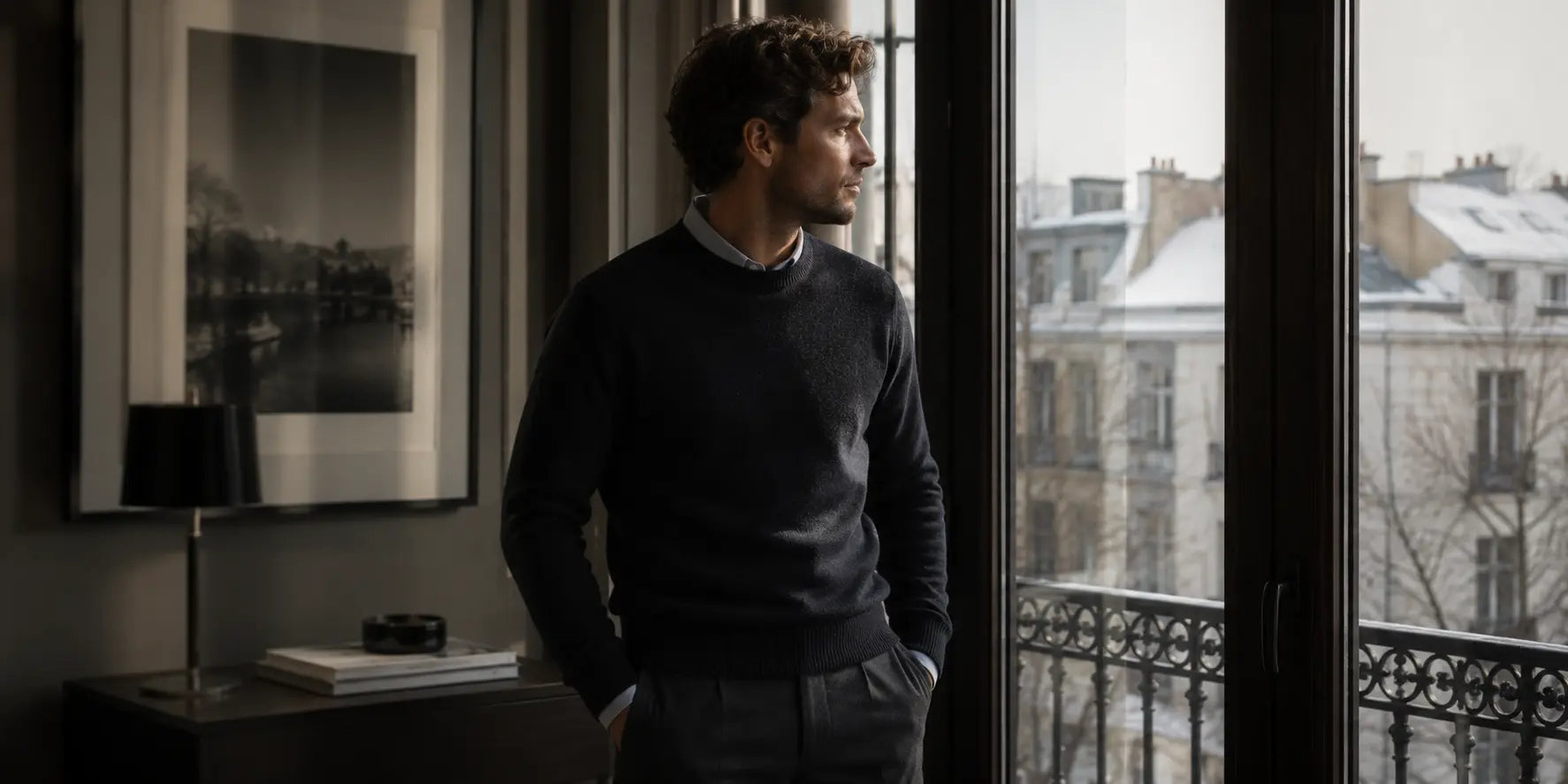 Hombre con jersey oscuro junto a una ventana en un ambiente elegante de invierno