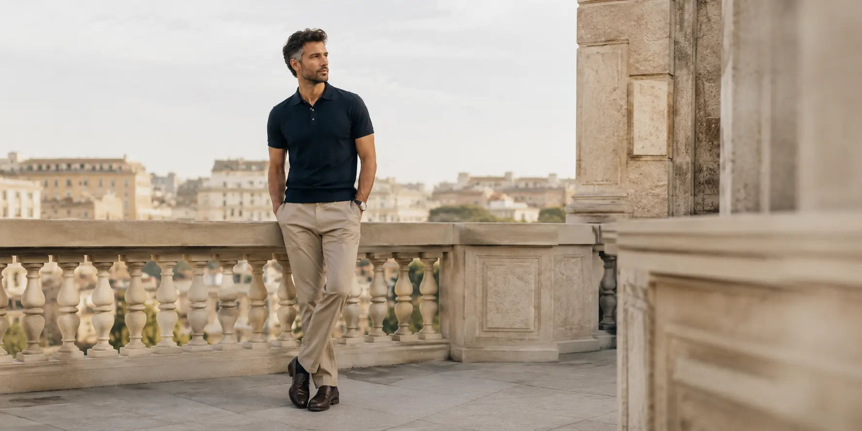 Hombre con polo azul marino y pantalón chino beige en una terraza urbana elegante