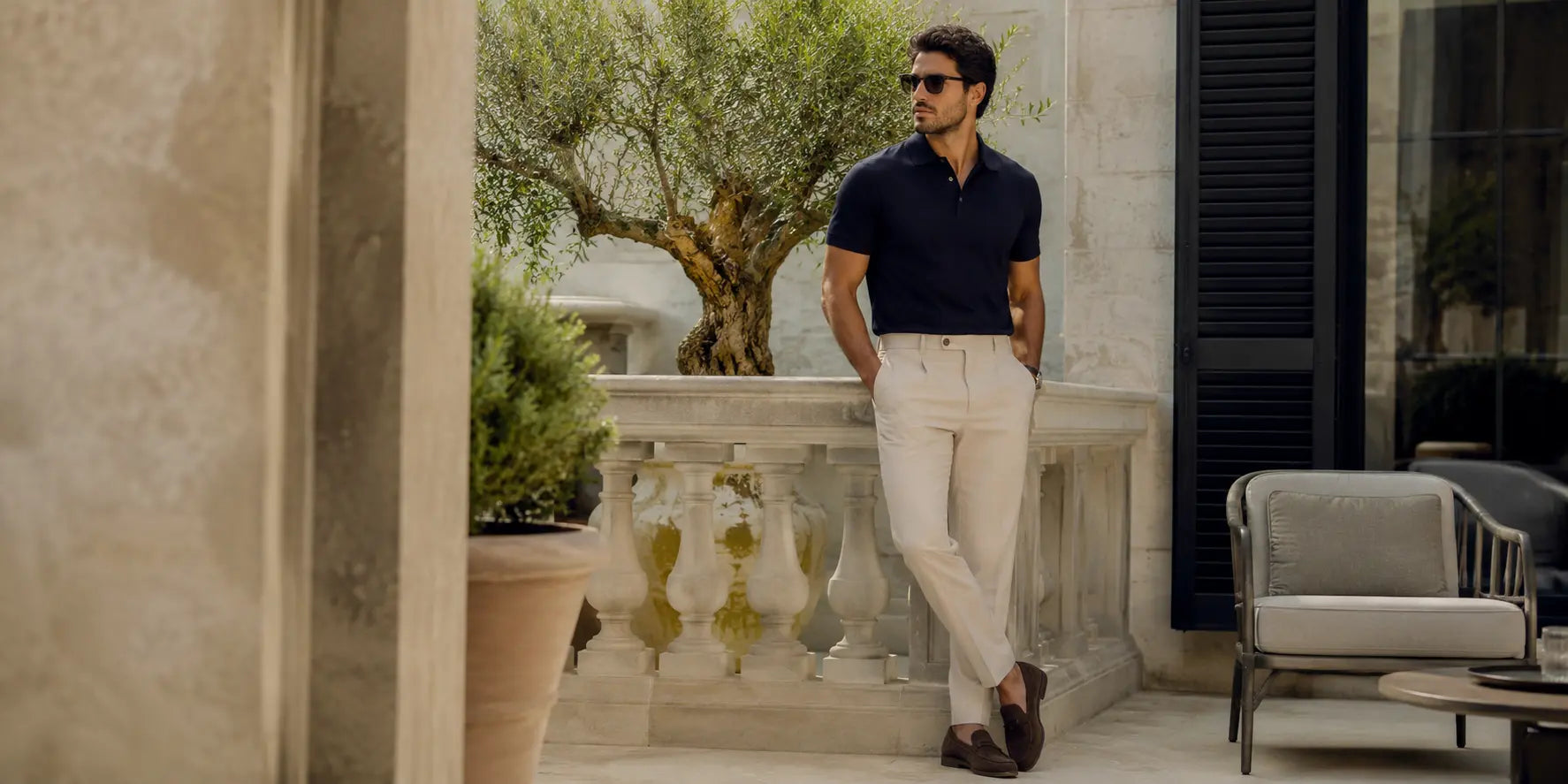 Hombre con polo azul marino y pantalón claro en una terraza elegante