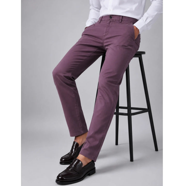 Hombre sentado en un taburete con pantalón chino granate Albano y camisa blanca.
